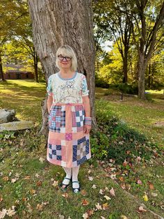 a woman standing in front of a tree wearing glasses and a dress with patches on it