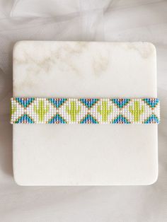 a beaded bracelet with blue, green and white beads sits on a marble surface