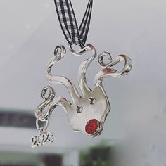 a silver pendant with a red stone in the shape of a frog on a black and white checkered ribbon