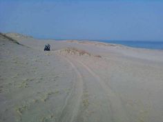 a four - wheeler driving on the beach in front of some sand dunes and water