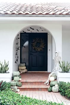 a black door with bats painted on it and pumpkins in the bushes around it