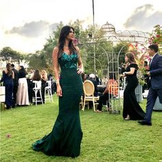 a woman in a green dress standing on top of a lush green field next to other people