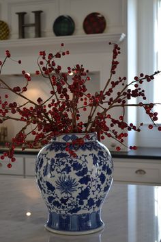 a blue and white vase with red berries in it sitting on a kitchen countertop