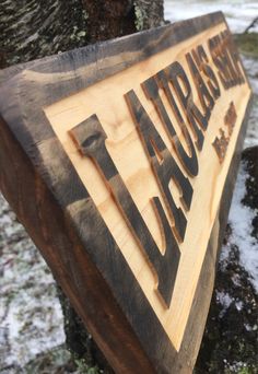 a wooden sign that is on the side of a tree in front of some snow