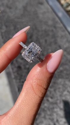 a woman's hand holding an engagement ring in front of her face and the other hand