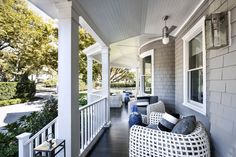 a porch with white wicker furniture and blue pillows on it's front porch