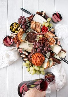 a platter filled with cheeses, meats and fruit next to wine glasses