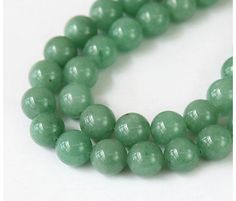 a close up of a necklace with green beads on a white surface and one bead has a silver clasp