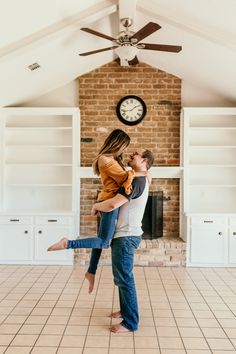 a man holding a woman in his arms while they are standing in front of a clock