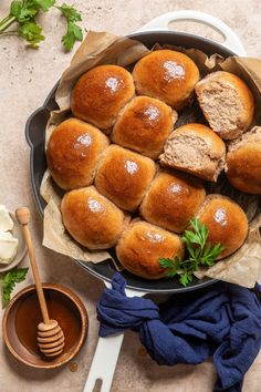 bread rolls in a pan with honey and parsley next to it on a table