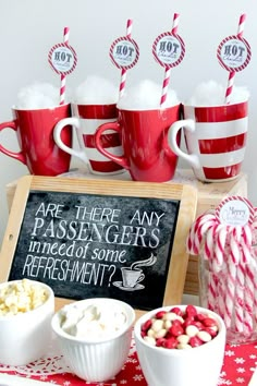 red and white candy canes are on the table next to cups with marshmallows in them