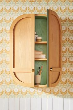 a wooden cabinet with two doors open in front of a wallpapered wall