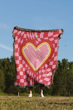 a large red and white checkered blanket with the word love on it in front of trees