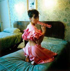 a woman in a pink dress is sitting on a bed and playing the trumpet with her hands