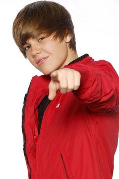 a young boy in a red jacket pointing at the camera with one hand and his thumb out