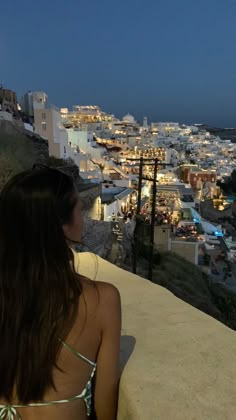 a woman sitting on top of a balcony next to the ocean at night with city lights in the background