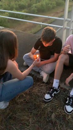 three young people sitting on the ground with one holding a lit candle in their hands