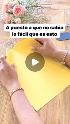 a woman is cutting paper on top of a table with scissors and flowers in the background