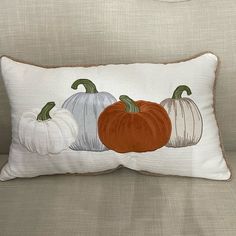 three pumpkins on a white pillow sitting on a couch