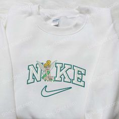 The Tinkerbell x Nike Cartoon Embroidered Sweatshirt is a delightful collaboration between two iconic brands. Featuring Tinkerbell, the beloved Disney character, intricately embroidered on a cozy sweatshirt, this piece is a must-have for any Disney enthusiast. The vibrant colors and high-quality stitching bring the magical world of Disney to life. Made with premium materials, this sweatshirt offers both comfort and style. Whether you’re a fan of Tinkerbell or simply love unique and eye-cat Embroidered Nike Crewnecks, Nike Embroidered Sweatshirt, Nike Cartoon, Disney Character Shirts, Nike Inspired, Nike Sweatshirt, Shirt Embroidery, Nike Sweatshirts, Inspirational Celebrities