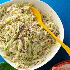 a white bowl filled with coleslaw on top of a blue table next to two plates