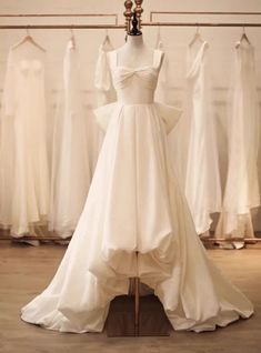 a white wedding dress is on display in front of some other gowns and dresses