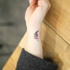 a woman's wrist with a small purple flower tattoo on the left side of her arm