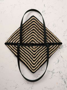 a black and tan woven bag on a white marble counter top with a black strap