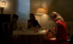 three women sitting at a table in a dimly lit room, eating and drinking wine