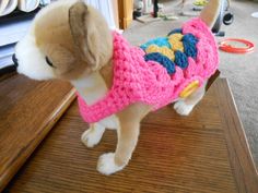 a small dog wearing a pink crocheted sweater on top of a wooden table