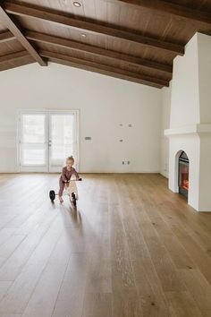 a young child riding on top of a skateboard in an empty room next to a fire place