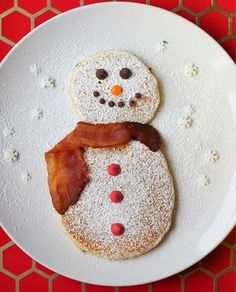 a white plate topped with two pancakes covered in powdered sugar, bacon and snowmen