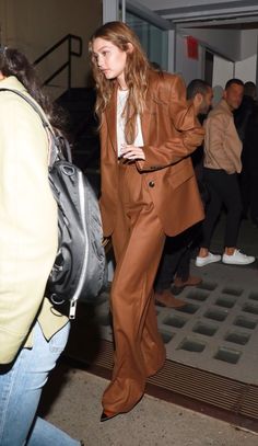 a woman in a brown suit and white shirt is walking down the street with her hand on her hip