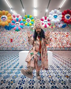 a man with long hair wearing a hat and trench coat standing in front of balloons