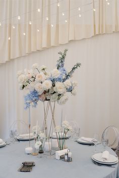 a blue table cloth with white flowers and silver place settings on it is set for a formal dinner