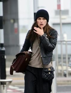 a woman walking down the street with her hand on her hip and wearing a black hat