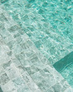 an umbrella sitting on the edge of a swimming pool next to a tiled wall and floor