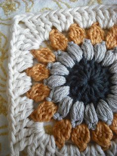 a crocheted square with an orange, white and black flower in the center