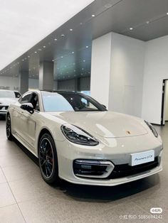 a white porsche panamera parked in a showroom with other cars behind it