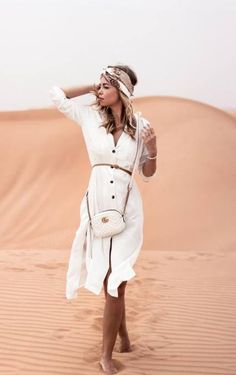 a woman standing in the desert wearing a white dress and headband with her hand on her hip