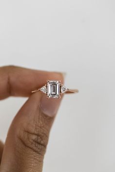 a woman's hand holding an emerald and diamond ring