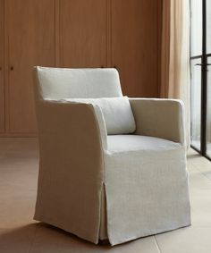 a white chair sitting on top of a tile floor next to a wooden cabinet and window