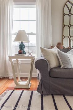 a living room with a couch, mirror and lamp on the table in front of it