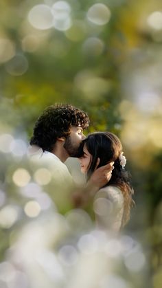 a man and woman kissing each other in front of some trees with boket