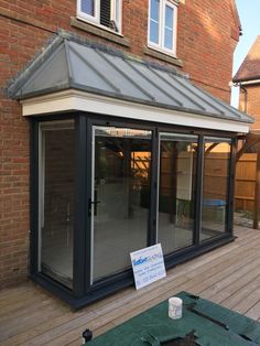 a glass enclosed patio area with a sign on the table next to it and a brick building in the background