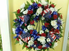 a wreath with red, white and blue flowers is hanging on the front door for memorial day