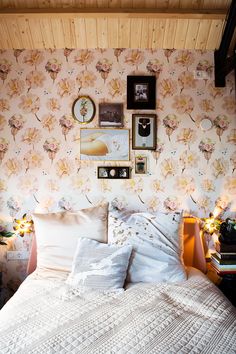 a bedroom with floral wallpaper and white bedding, framed pictures on the wall