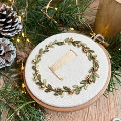 a close up of a embroidery on a wooden surface with pine cones and evergreen needles