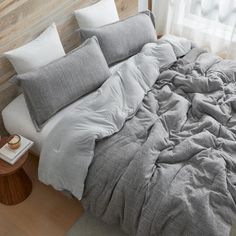 an unmade bed with grey linens and pillows