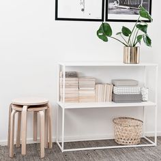 a white shelf with books and a plant on it next to two pictures hanging on the wall